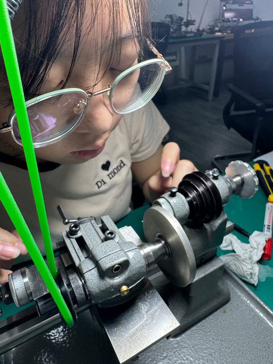 A student in glasses leaning in over the lathe, the green drive belt crossing the frame, the headstock and chuck in focus