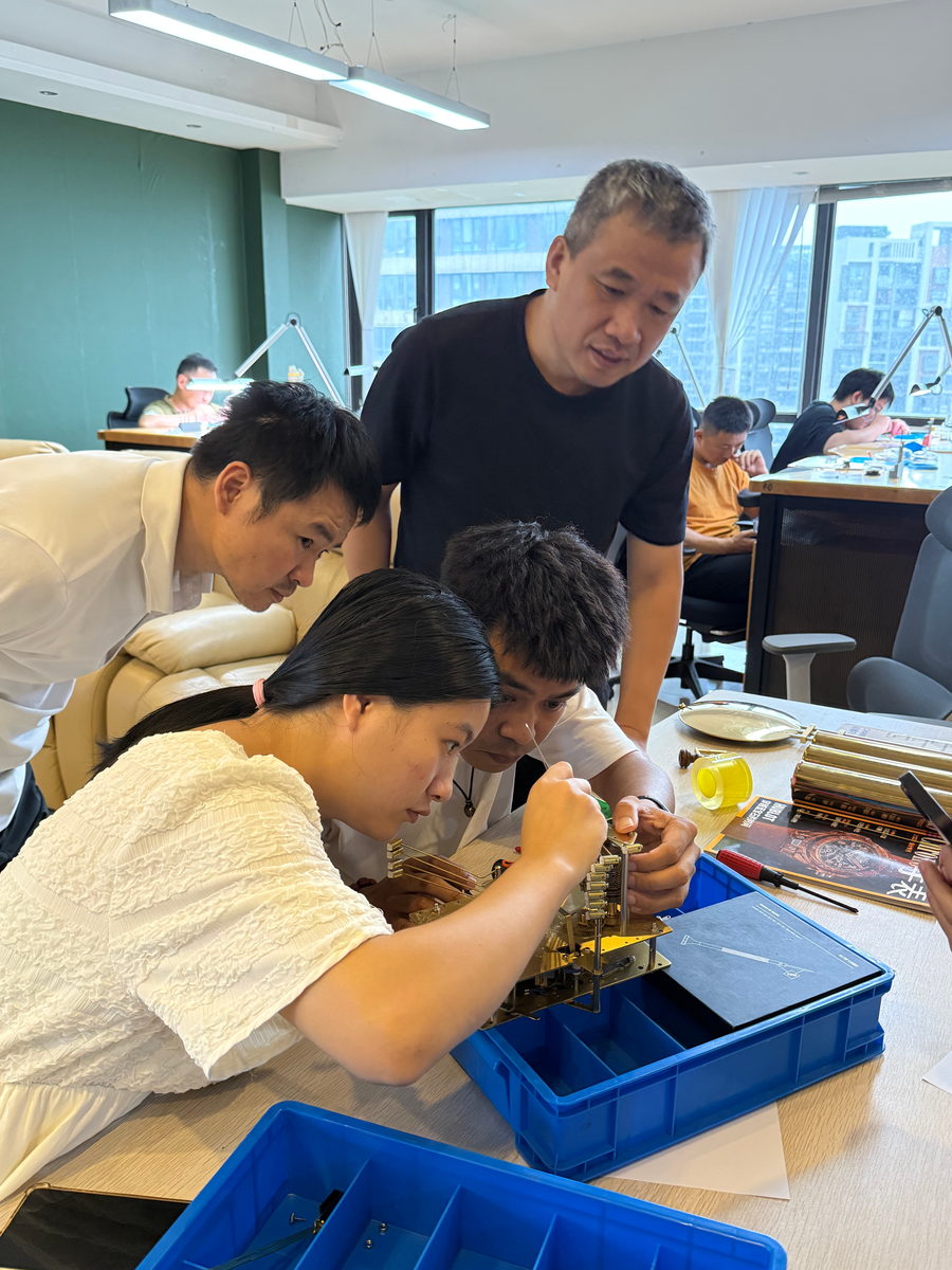 An instructor leaning over a student's shoulder to correct his work on a clock movement